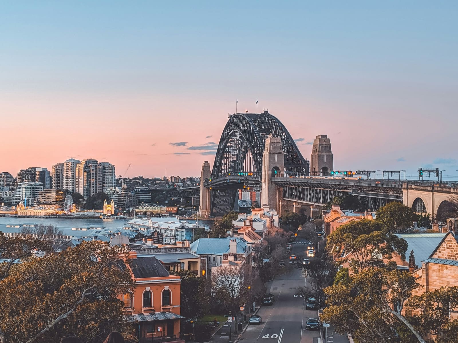 The Sydney Harbour Bridge seen from the water at sunset, with the city skyline behind it